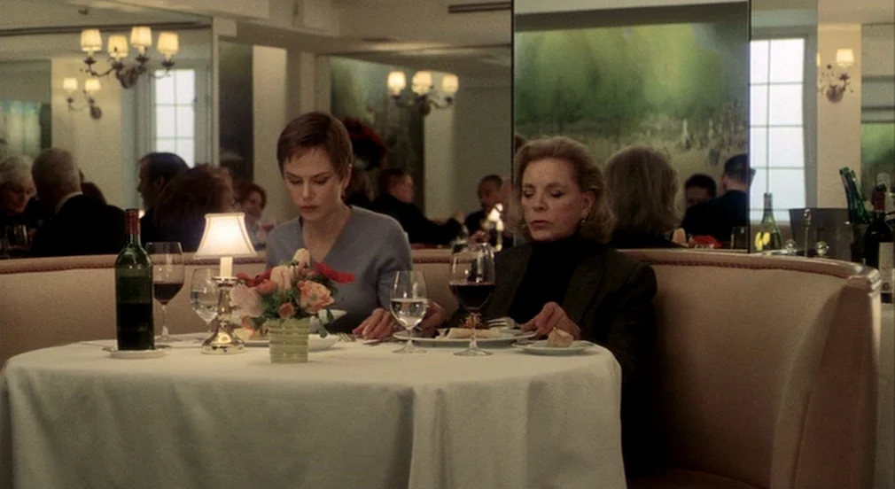Birth (2004) movie still: medium — A restaurant booth with white tablecloths and reflective mirror panels on the back walls. Two women dine at the…