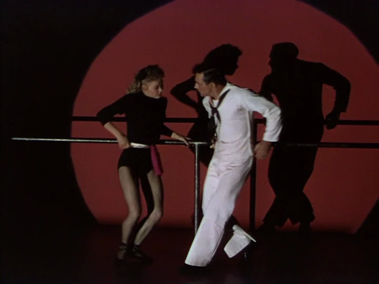 On The Town (1949) movie still: fullbody — A dance studio set features a stark red circular light against a black background. A woman in a black…
