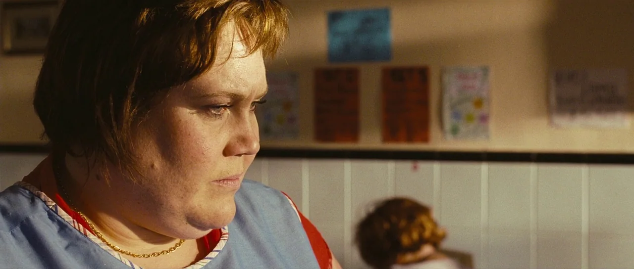 Eden Lake (2008) movie still: closeup — The wall behind the subject features white tiles and several colorful posters. A middle-aged woman looks…