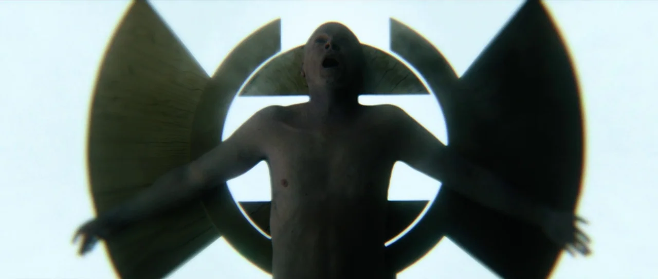 Hellraiser (2022) movie still: medium — A man is positioned within a large metallic circular structure against a bright background. He is shirtless…