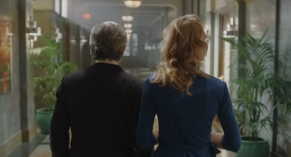 The Congress (2013) movie still: medium — A long, ornate hotel corridor features potted plants and dim ceiling lights. A man in a dark suit and a…