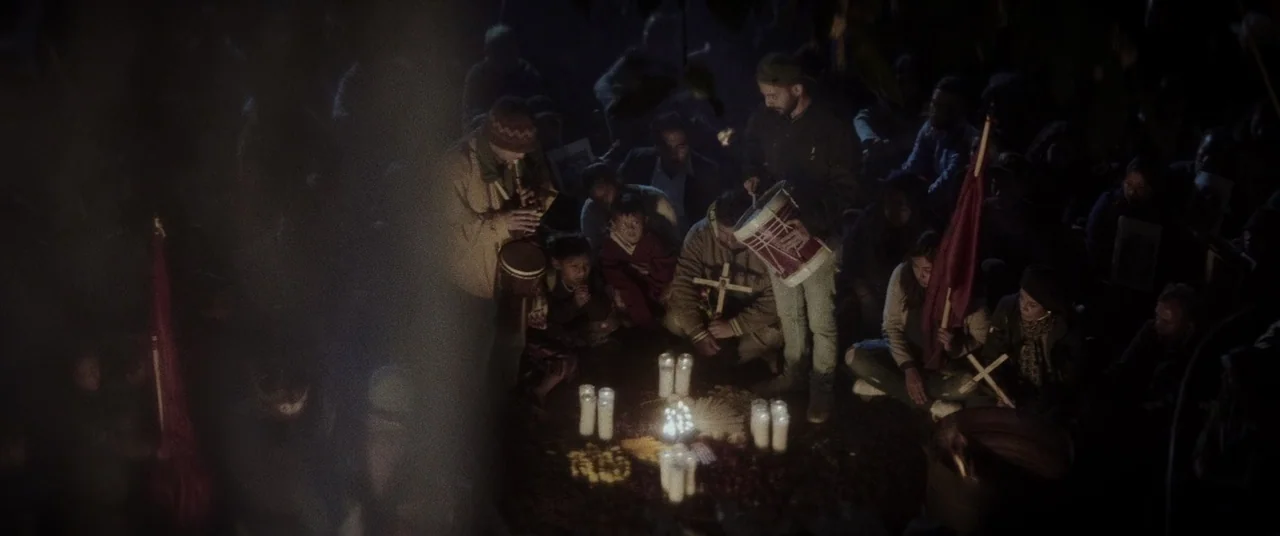 La Llorona (2019) movie still: wide — A group of people gathers at night in a dark outdoor space around candles. Musicians play drums and wind…