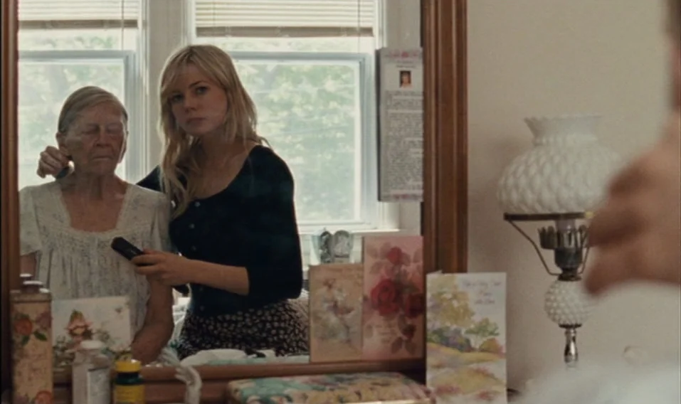 Blue Valentine (2010) movie still: medium — A reflection in a wooden vanity mirror shows a young woman tending to an elder. The mirror surface…