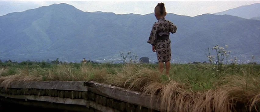 Lone Wolf and Cub: Baby Cart to Hades (1972) movie still: wide — An open field with tall, dry grass sits before a large mountain range. A young boy…