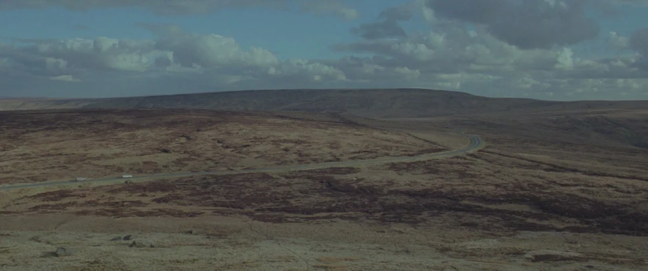 Catch Me Daddy (2014) movie still: establishing — A vast, rolling landscape of brown heather and dry grasses stretches toward distant hills. A thin,…