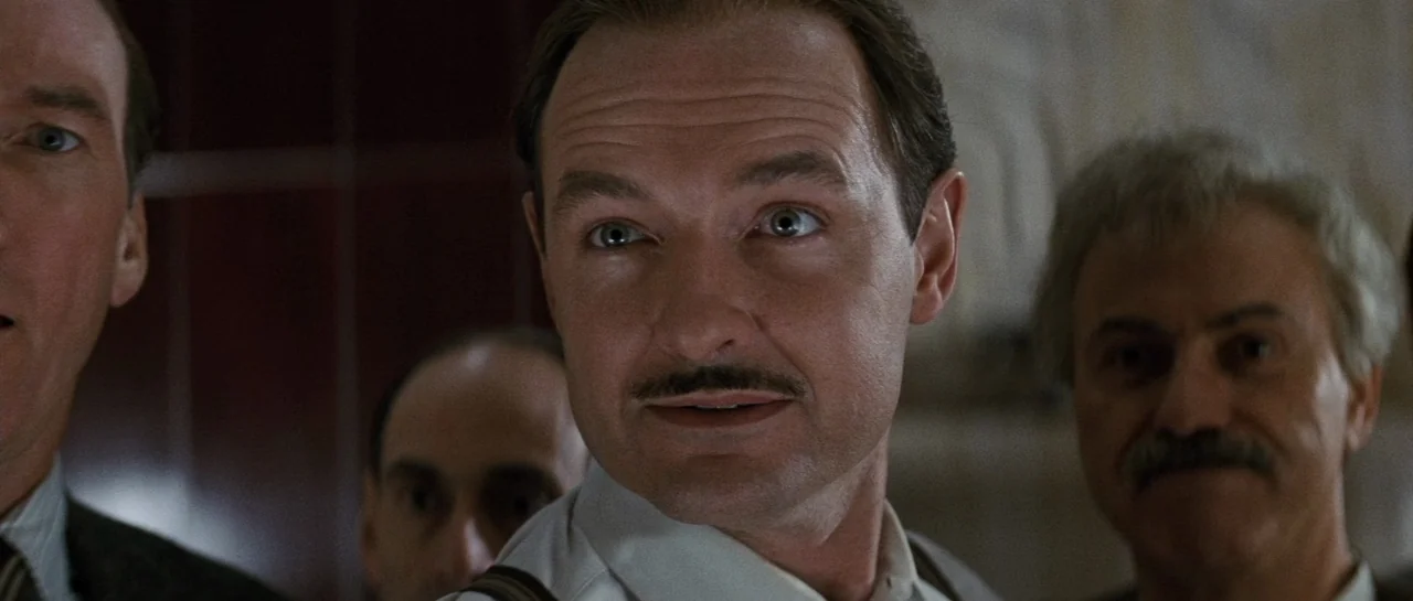 The Rocketeer (1991) movie still: closeup — Four men stand close together in what appears to be a dimly lit office. The central man with a mustache…