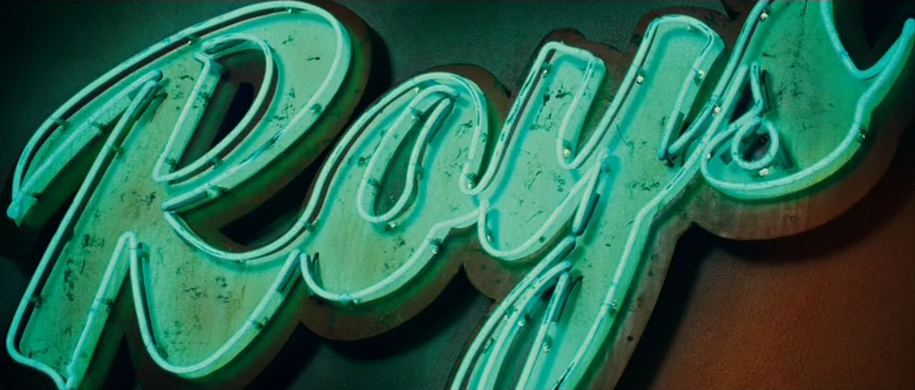 Paul (2011) movie still: closeup — A close-up view of a weathered teal neon sign spelling Ray's against a wall. The glass tubes are mounted on a…