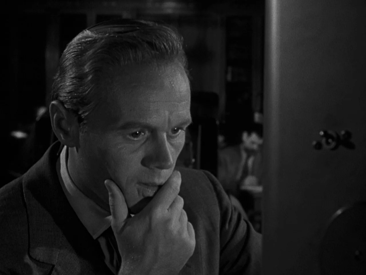 Pickup on South Street (1953) movie still: closeup — A dark office setting with shelves visible in the background and a metallic surface foreground.…