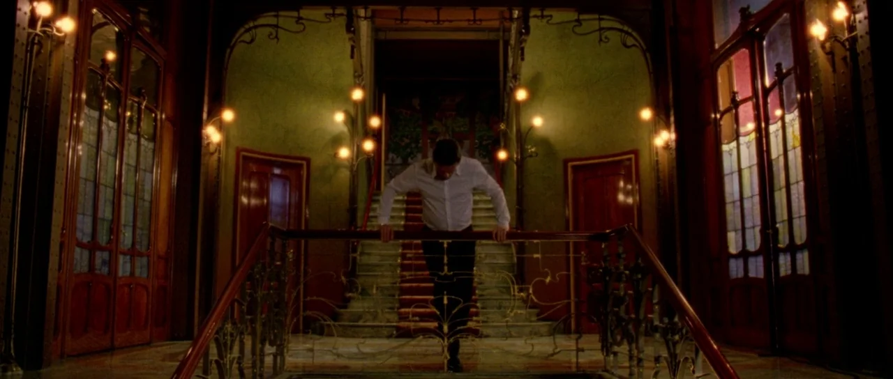 The Strange Colour of Your Body’s Tears (2013) movie still: wide — A grand, dim building interior features Art Nouveau wood paneling and ornate…