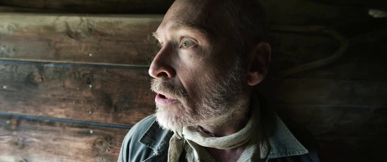 A Hidden Life (2019) movie still: closeup — A dark wooden room with thick horizontal timber walls shows a dimly lit interior. An elderly man with a…