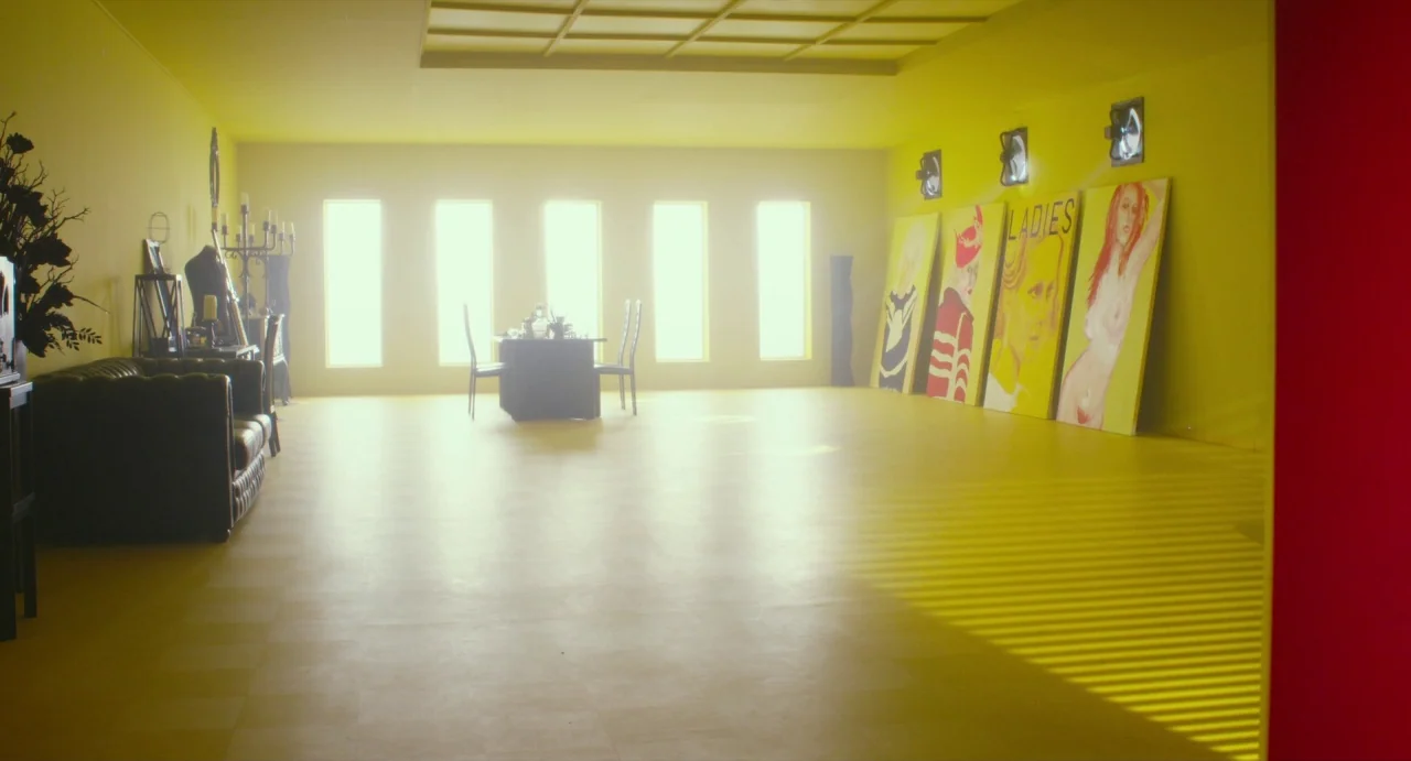 Making of: Antiporno (2016) movie still: wide — A spacious, vibrant yellow room contains several large figurative paintings leaned against the right…