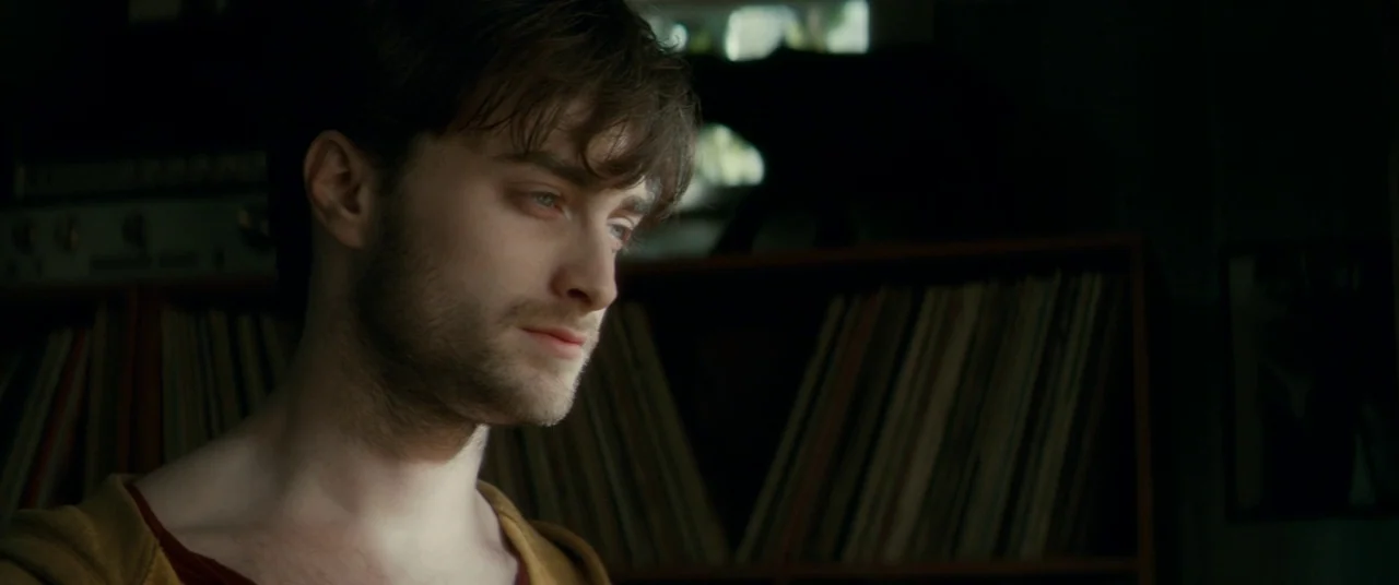 Horns (2013) movie still: closeup — A dimly lit room features shelves filled with organized vinyl records in the background. A young man with light…