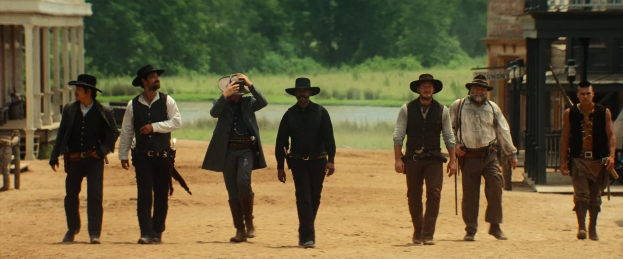 The Magnificent Seven (2016) (2016) movie still: fullbody — A dusty road in a 19th-century frontier town lined with wooden buildings. A group of six…