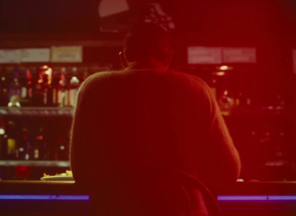 Laurence Anyways (2012) movie still: medium — A dark bar interior features rows of blurred bottles against a dimly lit back wall. A person in a knit…