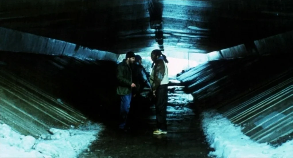 Narc (2002) movie still: wide — A dark concrete underpass is lined with snow and ice on the ground. Two men face each other in the center while a…