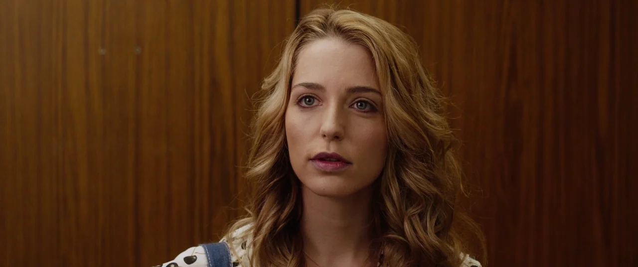 Happy Death Day (2017) movie still: closeup — A woman stands centered in front of vertically oriented wood-paneled elevator walls. She stares…