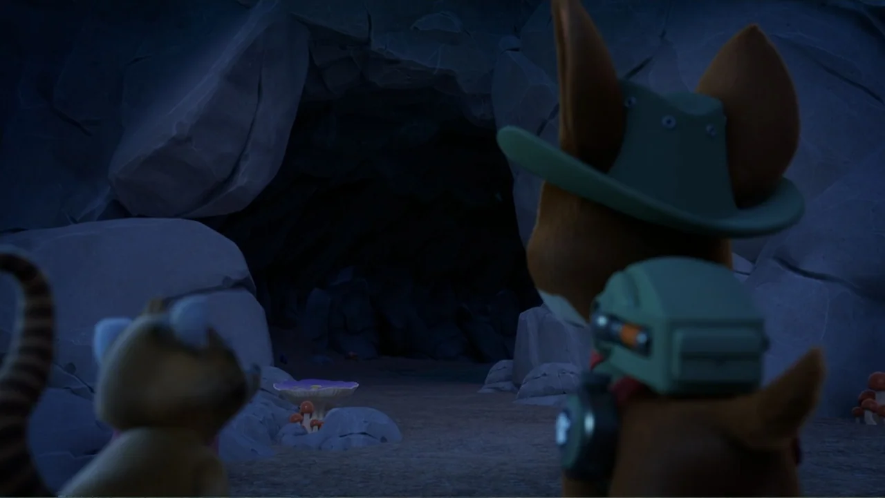 Valiente: A Tracker Story (2025) movie still: medium — A dark rocky cave mouth is surrounded by large grey stone formations and glowing mushrooms.…