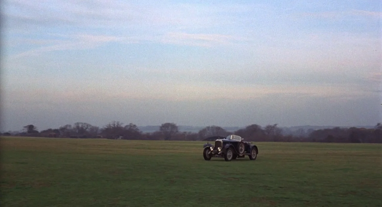 The Abominible Dr. Phibes (1972) movie still: wide — A vast, flat open field under a pale dusk sky extends toward distant trees. A vintage dark…