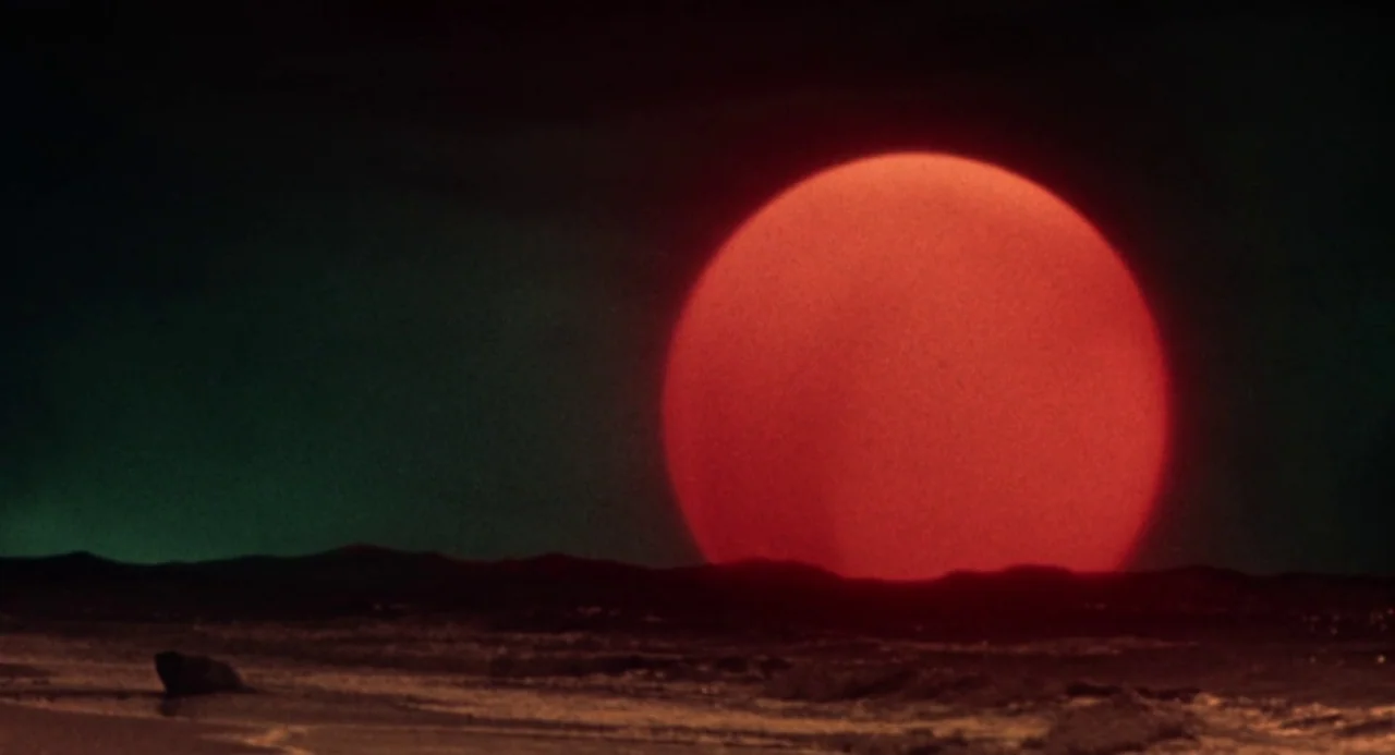 Queen of Blood (1966) movie still: wide — A dark, barren landscape is silhouetted against a massive, intensely red lunar body. A thin strip of light…