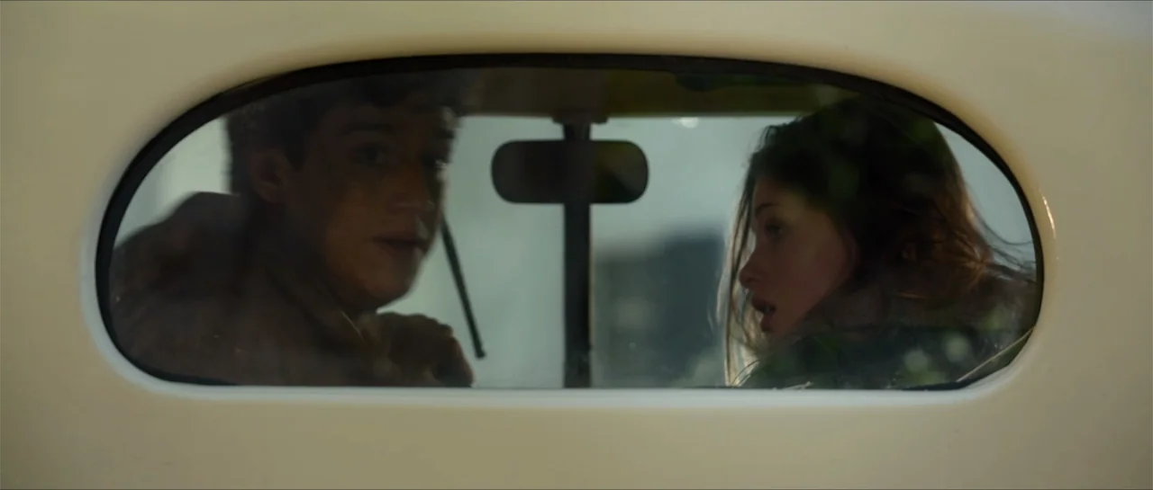 Jeepers Creepers 3 (2017) movie still: medium — A view through the back window of a car shows the interior cabin. A man and woman occupy the front…