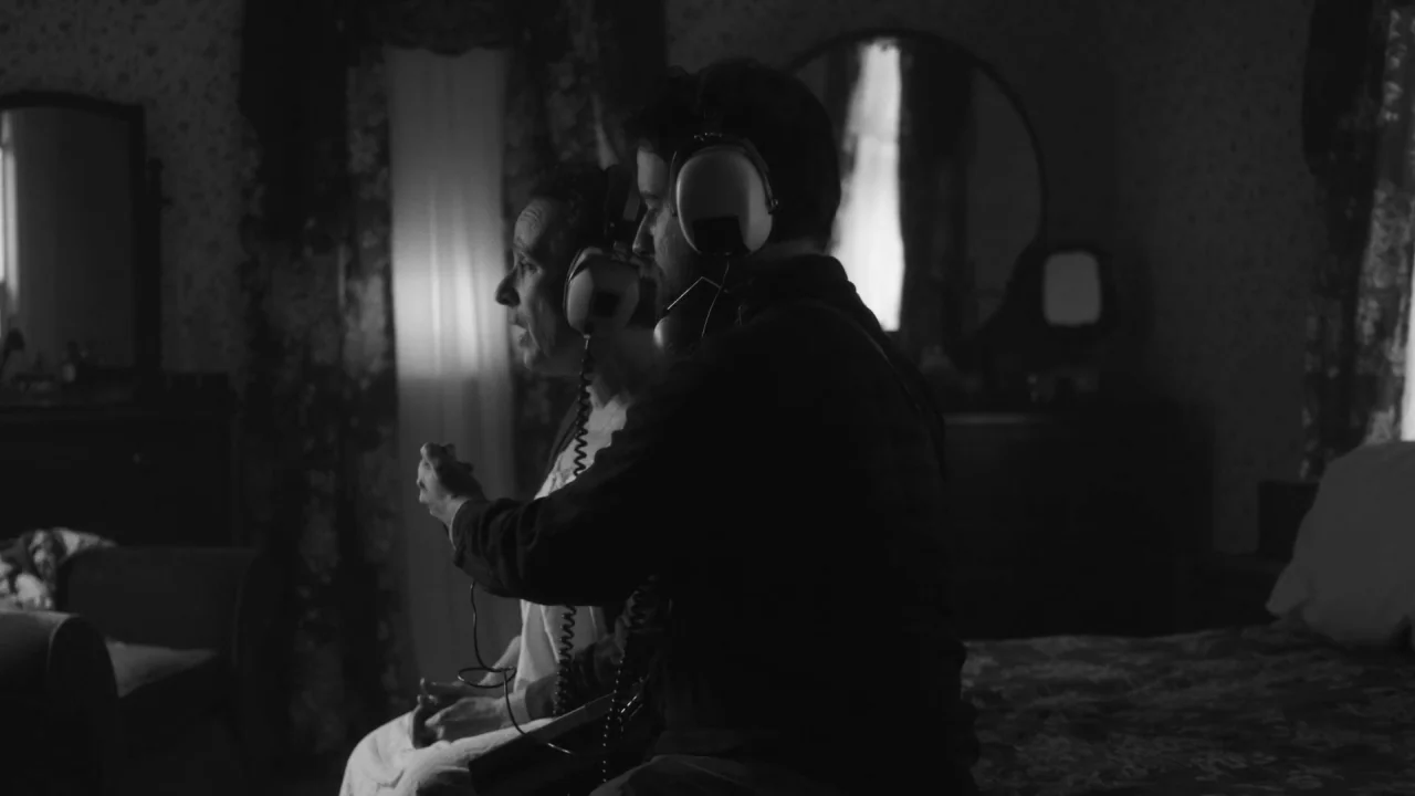 Collective: Unconscious (2016) movie still: medium — A dimly lit room with floral patterned wallpaper features a bed and a mirror. A man sits next…