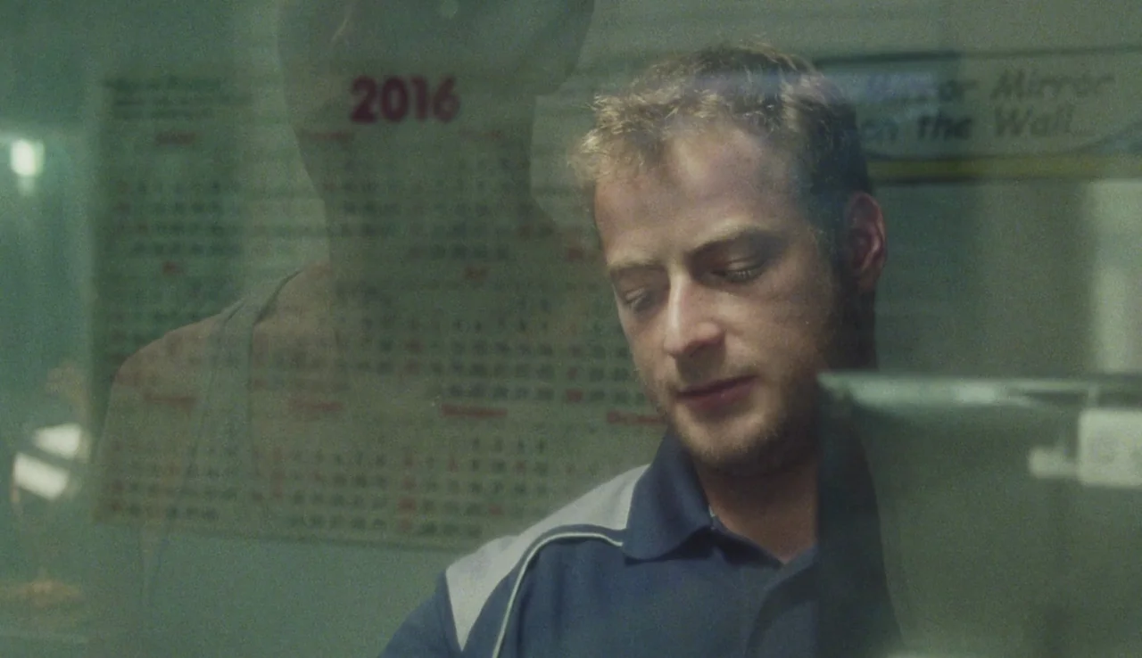 Beach Rats (2017) movie still: closeup — An interior space with a calendar reflecting on a glass surface in front. A young man wearing a polo shirt…