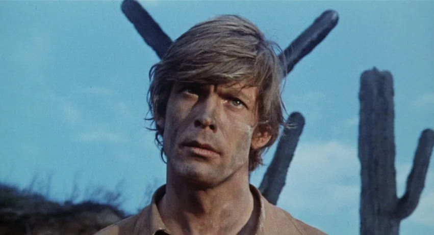 Roy Colt and Winchester Jack (1970) movie still: closeup — An arid desert environment with tall cacti positioned against a clear blue sky. A young…