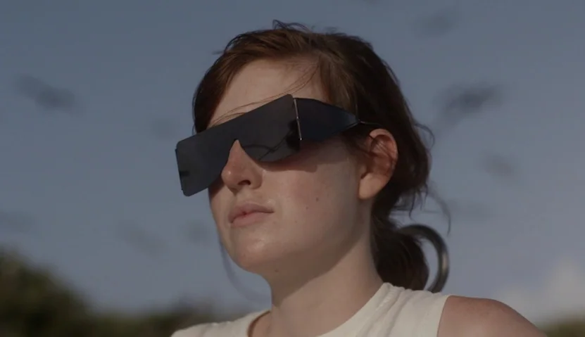 Kate Plays Christine (2016) movie still: closeup — A person stands outdoors during the daytime with a blurry sky and distant birds visible. The…