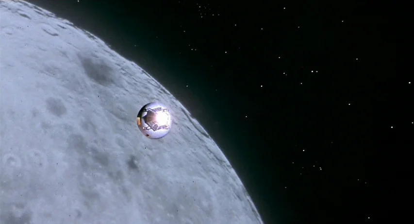 CQ (2001) movie still: wide — A small metallic spacecraft floats above the cratered, gray surface of the moon. The vast darkness of space filled…