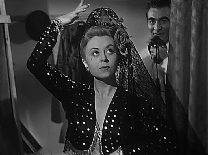 Variety Lights (1950) movie still: medium — A cramped dressing room features hanging garments in the background and a curtain divider. A woman in a…