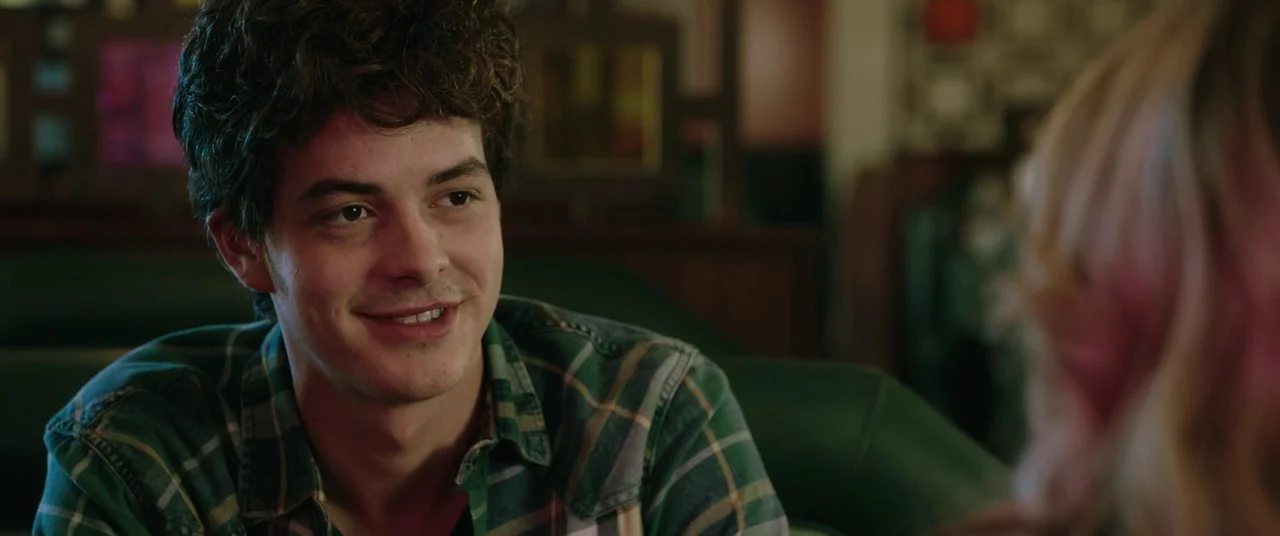 Happy Death Day (2017) movie still: medium — A man sits at a booth inside a dimly lit diner with green upholstery. He smiles while looking toward…