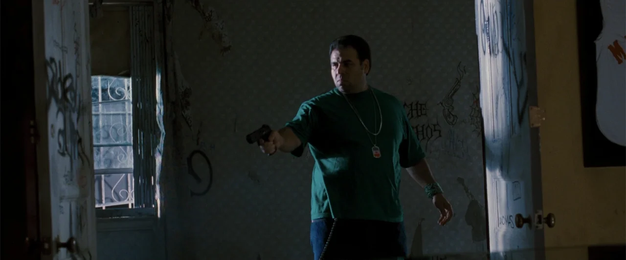 Cop Out (2010) movie still: medium — A dimly lit room features walls covered in dark graffiti and a barred window. A man in a green t-shirt stands…