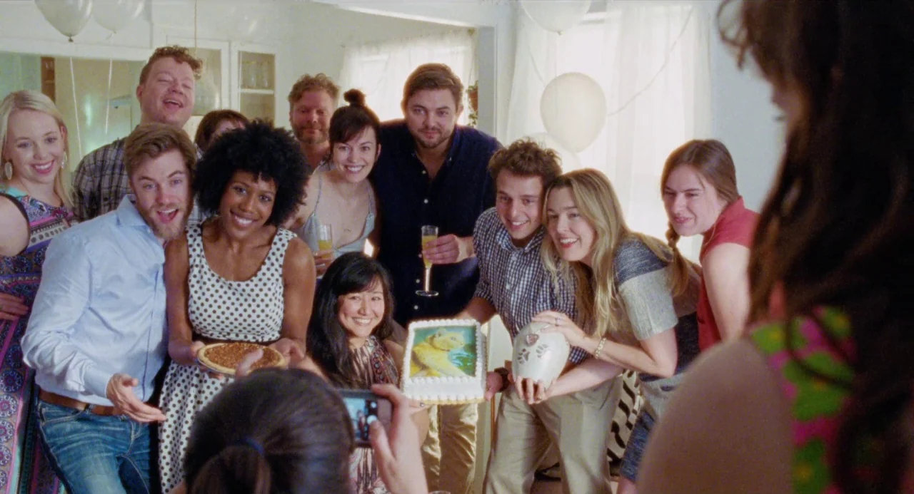 Mr. Roosevelt (2017) movie still: medium — A group of diverse young adults gather inside a brightly lit living room space. They smile at a person…