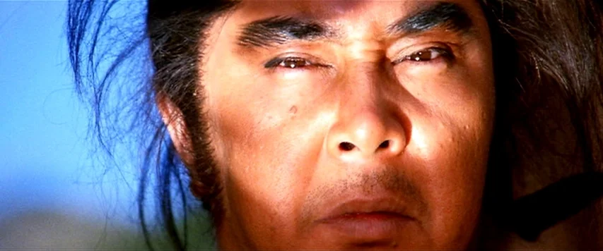 Lone Wolf and Cub: Sword of Vengeance (1972) movie still: closeup — A close-up view of a man standing outdoors against a clear blue sky. The…