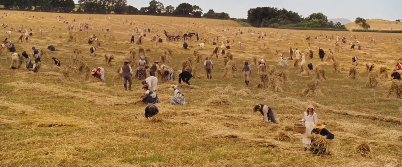 Far from the Madding Crowd (2015) movie still: wide — A vast, expansive wheat field is filled with many people working during the harvest. The…