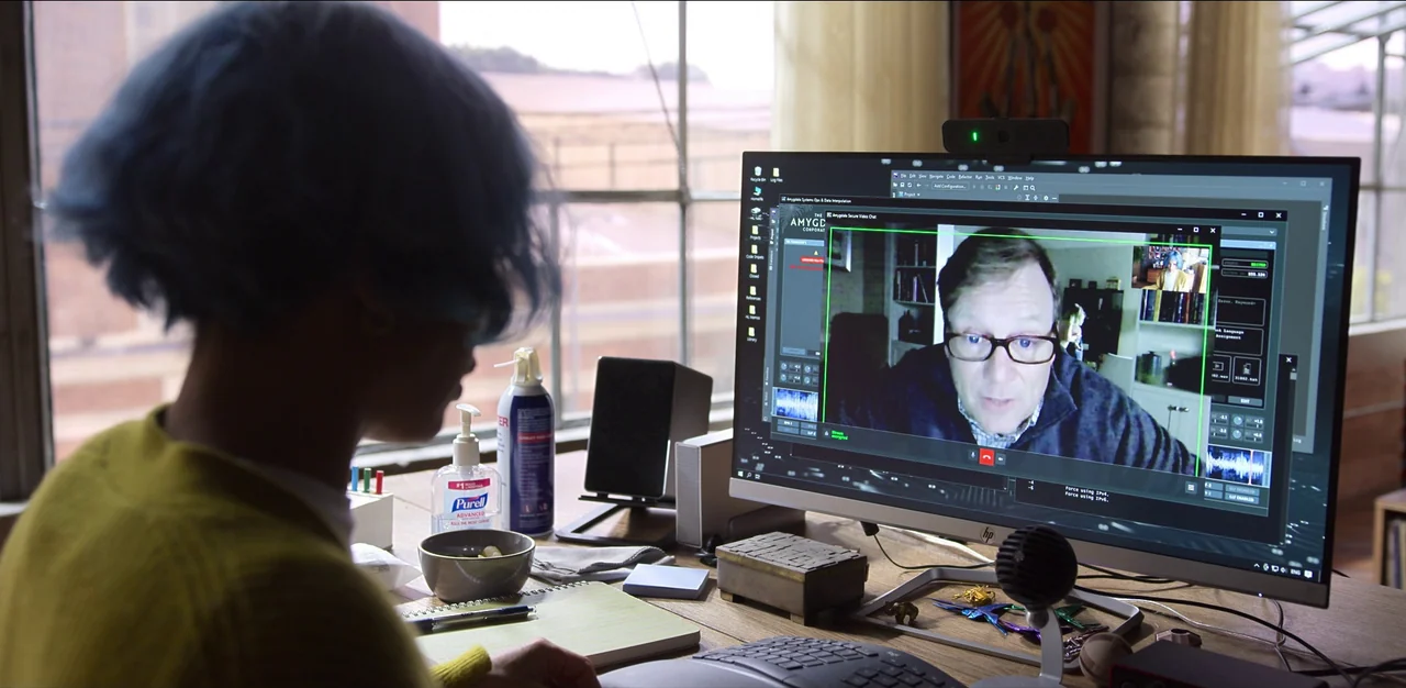 Kimi (2022) movie still: medium — An office workspace features a computer monitor displaying a video call on a desk. A person with blue hair sits…