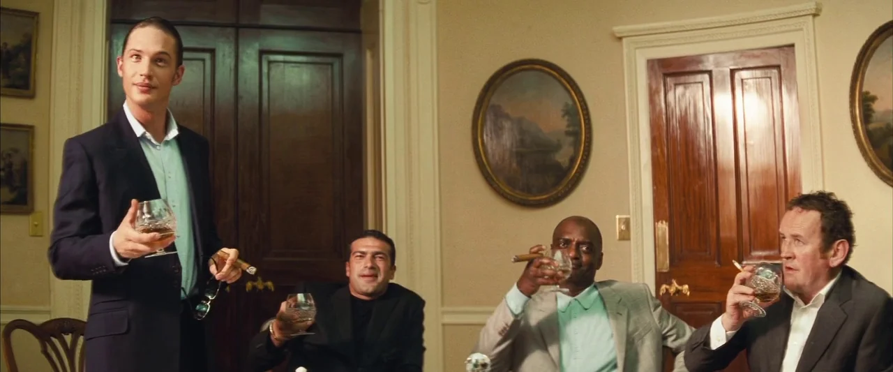Layer Cake (2004) movie still: medium — A well-lit formal room features dark wood doors and oval paintings on the wall. Four men gather around a…