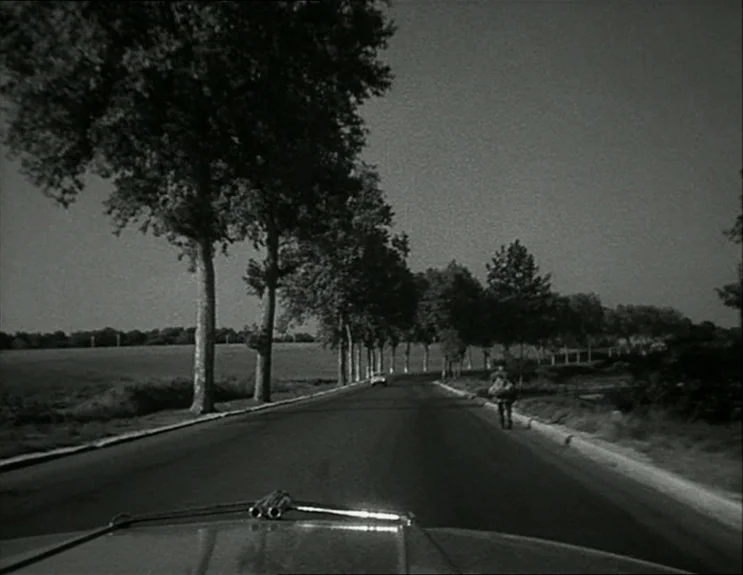 À Bout De Souffle (Breathless) (1960) movie still: wide — A long, asphalt road winds through a flat rural landscape lined with mature trees. A lone…