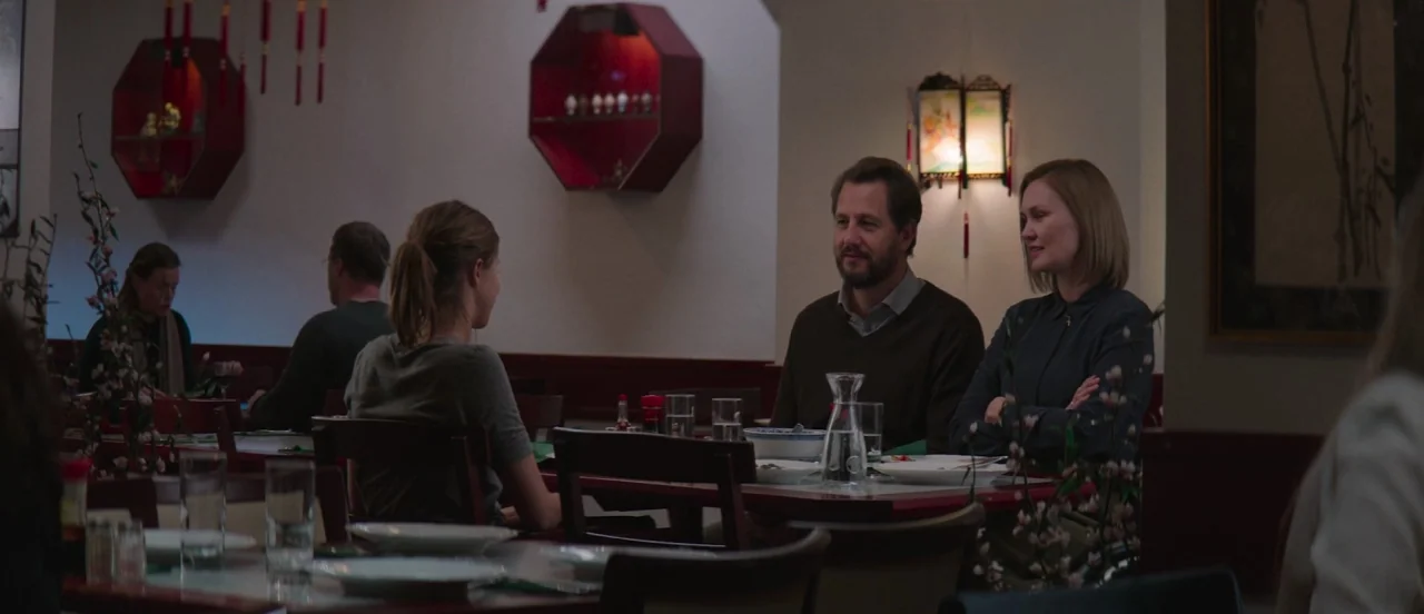 Thelma (2017) movie still: medium — An Asian-themed restaurant with octagonal wall displays and wooden chairs around tables. A middle-aged couple at…
