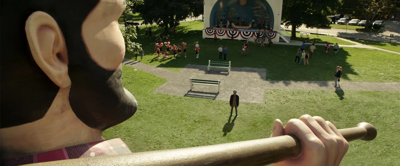 K.G.F: Chapter 2 (2022) movie still: wide — A sunny public park features a central bandstand with red and white bunting. A lone man stands in the…