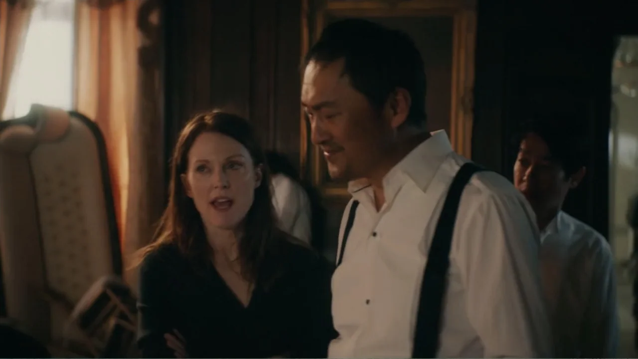 Bel Canto (2018) movie still: medium — A dimly lit interior space with classic wooden furniture and a large window. A man in suspenders and a woman…