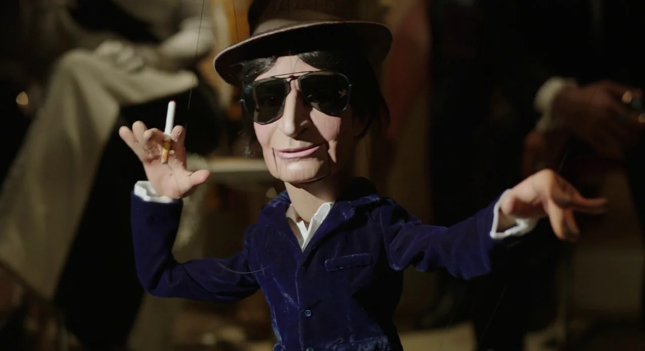 A Glimpse Inside The Mind Of Charles Swan III (2013) movie still: closeup — A miniature wooden puppet with dark hair and sunglasses stands on a dark…