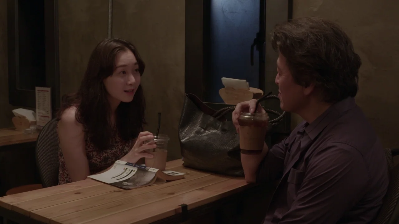 Yourself and Yours (2016) movie still: medium — A small indoor cafe table is occupied by a man and a woman. The two people converse while holding…