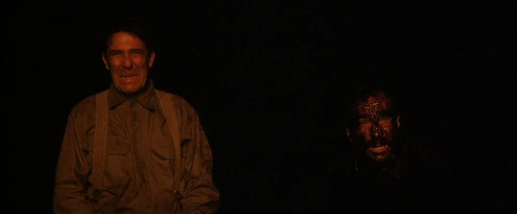 There Will Be Blood (2007) movie still: medium — A dark, void-like exterior setting at night with two men standing side by side. One man is clean…