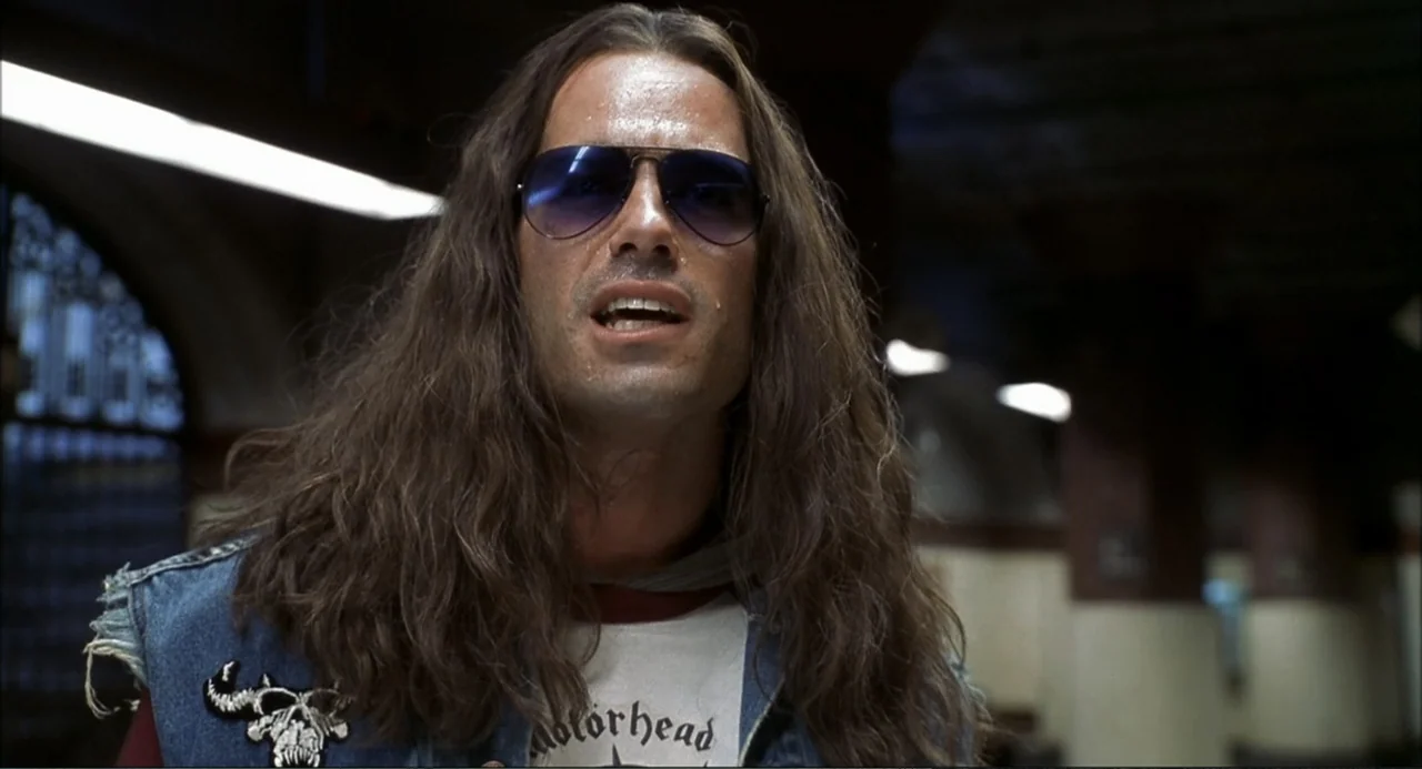 Little Nicky (2000) movie still: medium — A subway platform features tiled walls and metal structural supports in the background. A man with long…
