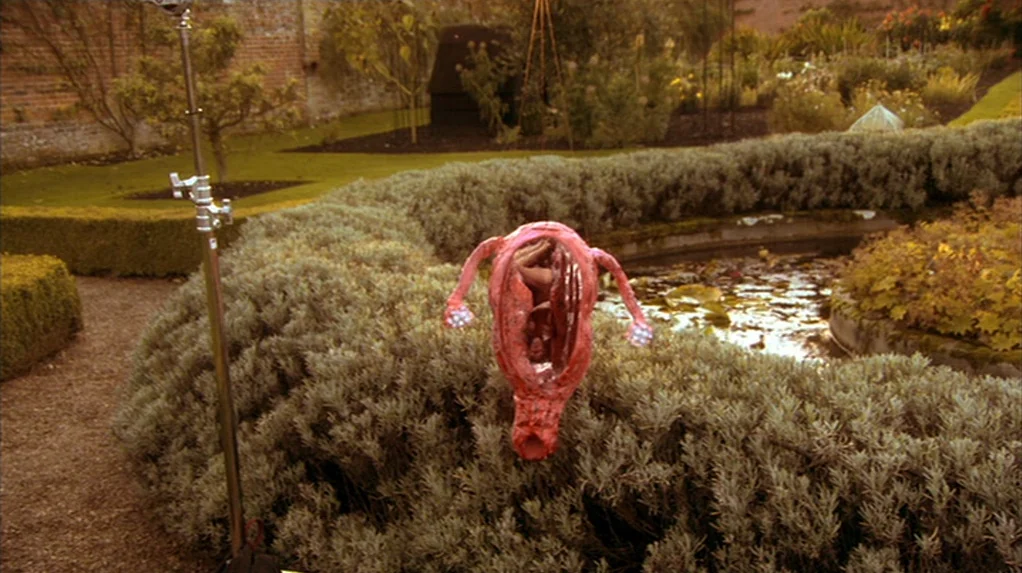 A Cock and Bull Story (2005) movie still: wide — A manicured formal garden features low trimmed hedges surrounding a stone-lined koi pond. A large…
