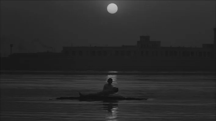 Death By Hanging (1968) movie still: wide — A dark river scene under a bright moon with a silhouette of a building. Two figures occupy a small patch…