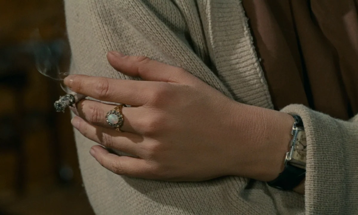 Muriel (1963) movie still: closeup — A close-up view shows a hand wearing an opal ring and a leather-strapped watch. The hand holds a cigarette that…