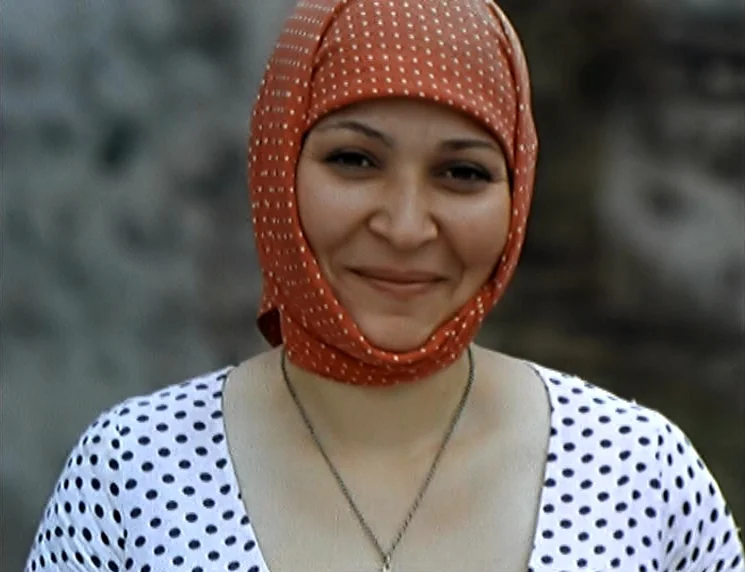 The Wishing Tree (1977) movie still: closeup — An outdoor rural setting provides a blurred, neutral background behind the woman. The woman stares…