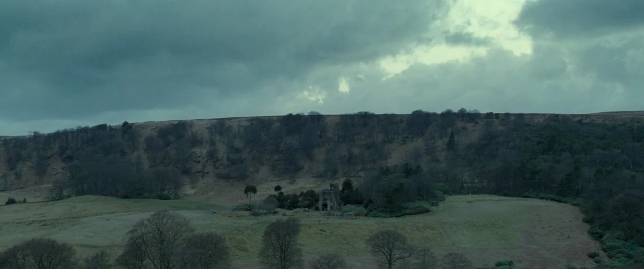 Catch Me Daddy (2014) movie still: establishing — A vast, open moorland sits under a heavy, overcast gray sky. The landscape features rolling hills…